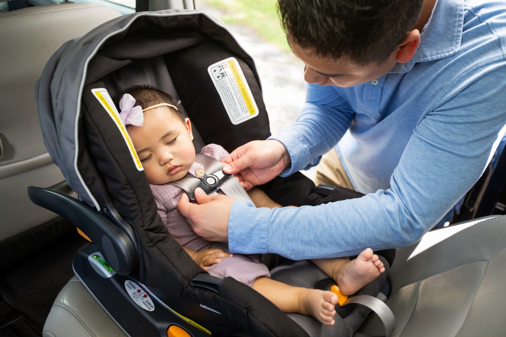 A dark-haired man, buckling a sleeping asian baby girl into a rear-facing infant car seat.